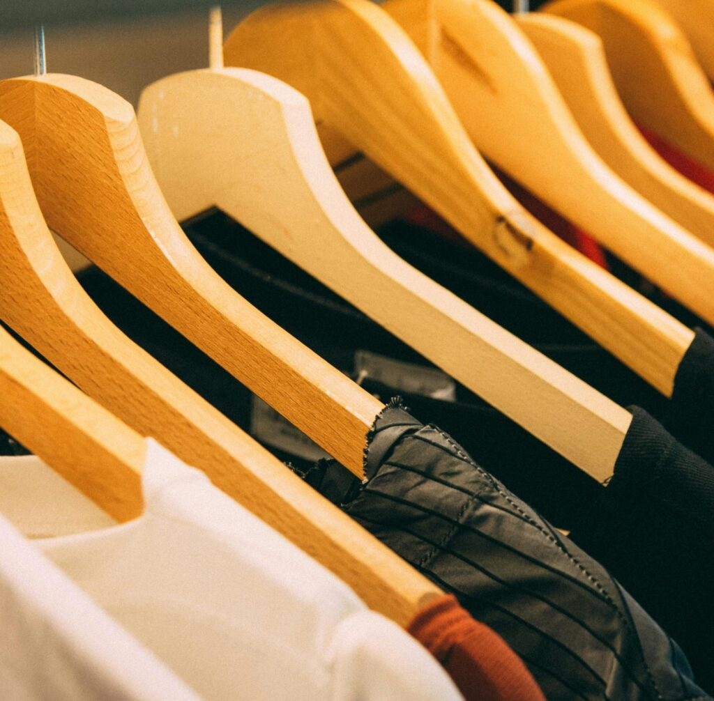 A close-up view of a row of clothes on wooden hangers, showcasing various fabrics and colors in a wardrobe setting.